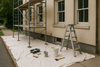 image of an outdoor building near a sidewalk, ground covered by canvas drop cloth and a scaffolding for painters near the buildings window.